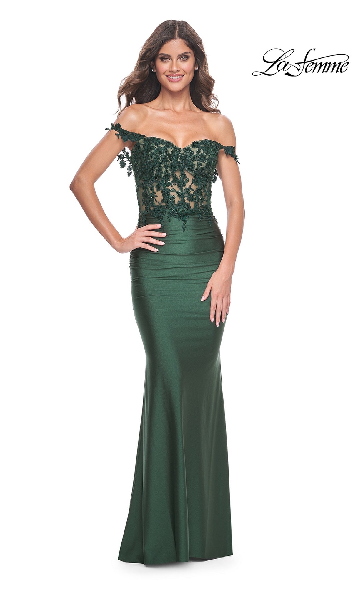 A woman poses with one hand on her hip in the La Femme Off-the-Shoulder Long Prom Dress 32302, a dark green gown featuring beaded floral lace on the bodice, set against a white background.
